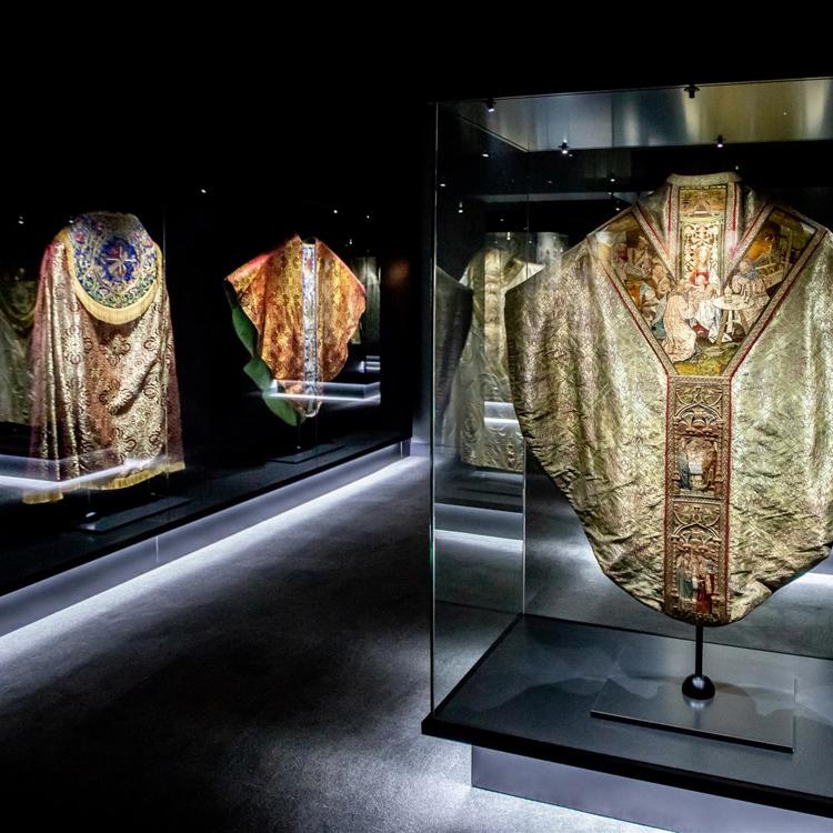 Donkere galerie met kerkelijke kleding achter glas